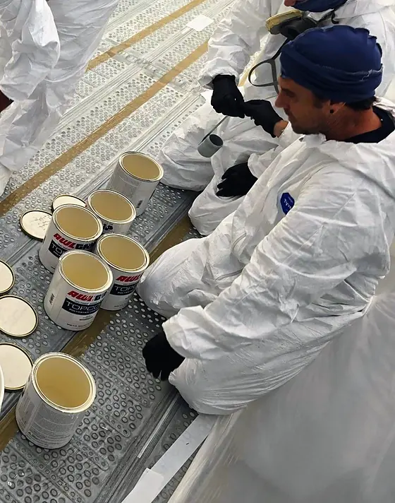 Latas abiertas de Awlgrip Topcoat en fila sobre la plataforma del andamio, dentro de la carpa