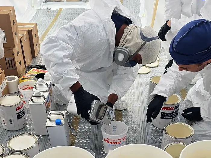 Pintor midiendo líquido en un vaso de mezcla junto a latas de Awlgrip Topcoat