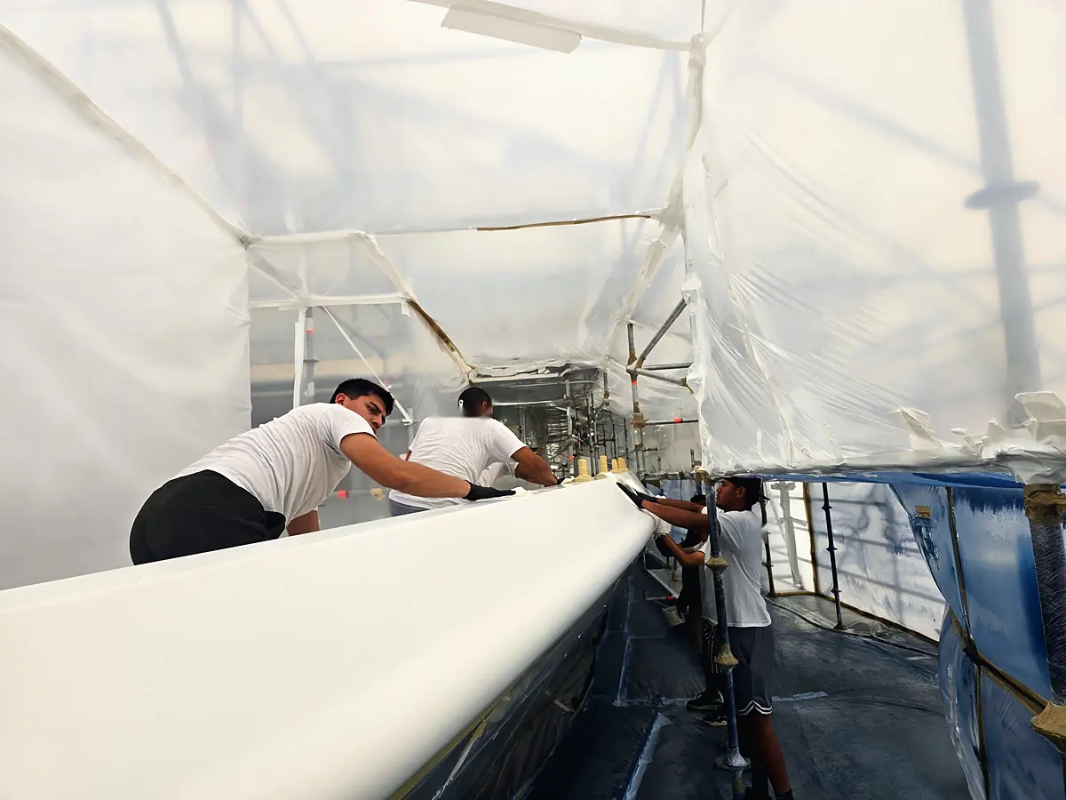 Crew sanding a white hull inside a containment tent